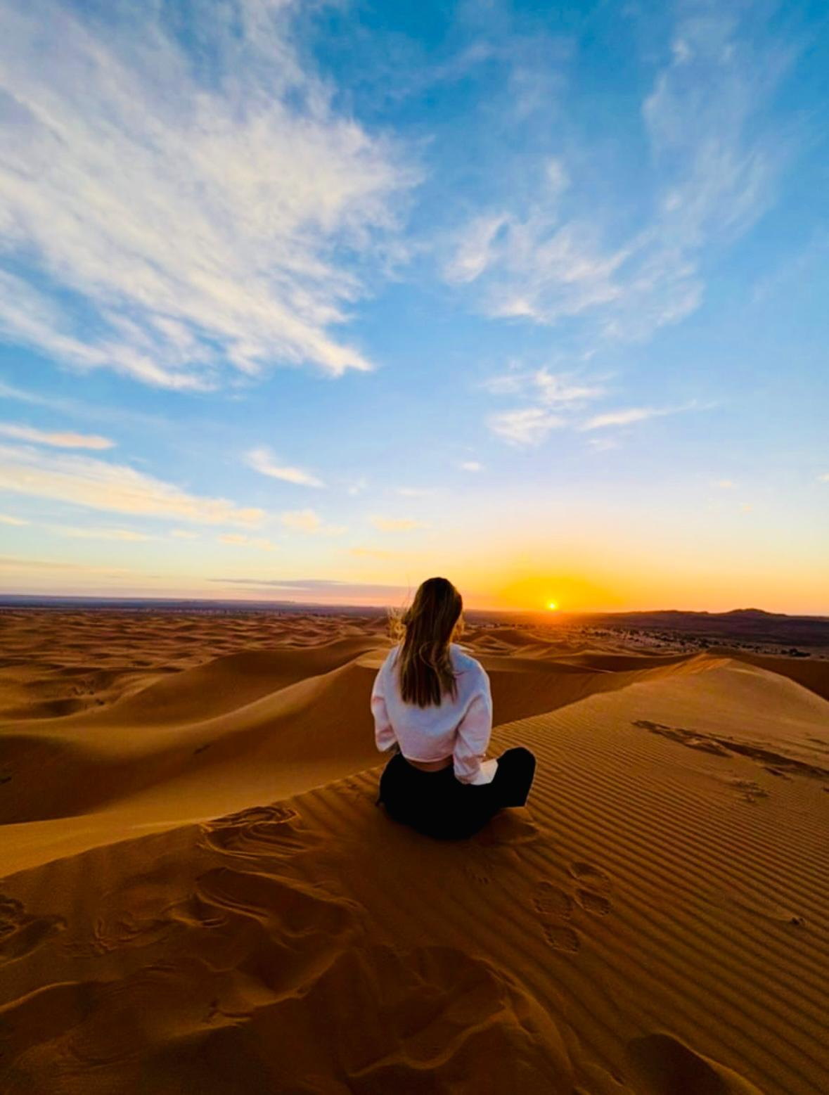 Viajera contemplando el amanecer sentada en lo alto de una duna