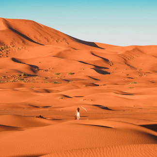 Una persona diminuta caminando entre las grandes dunas del Erg Chebbi